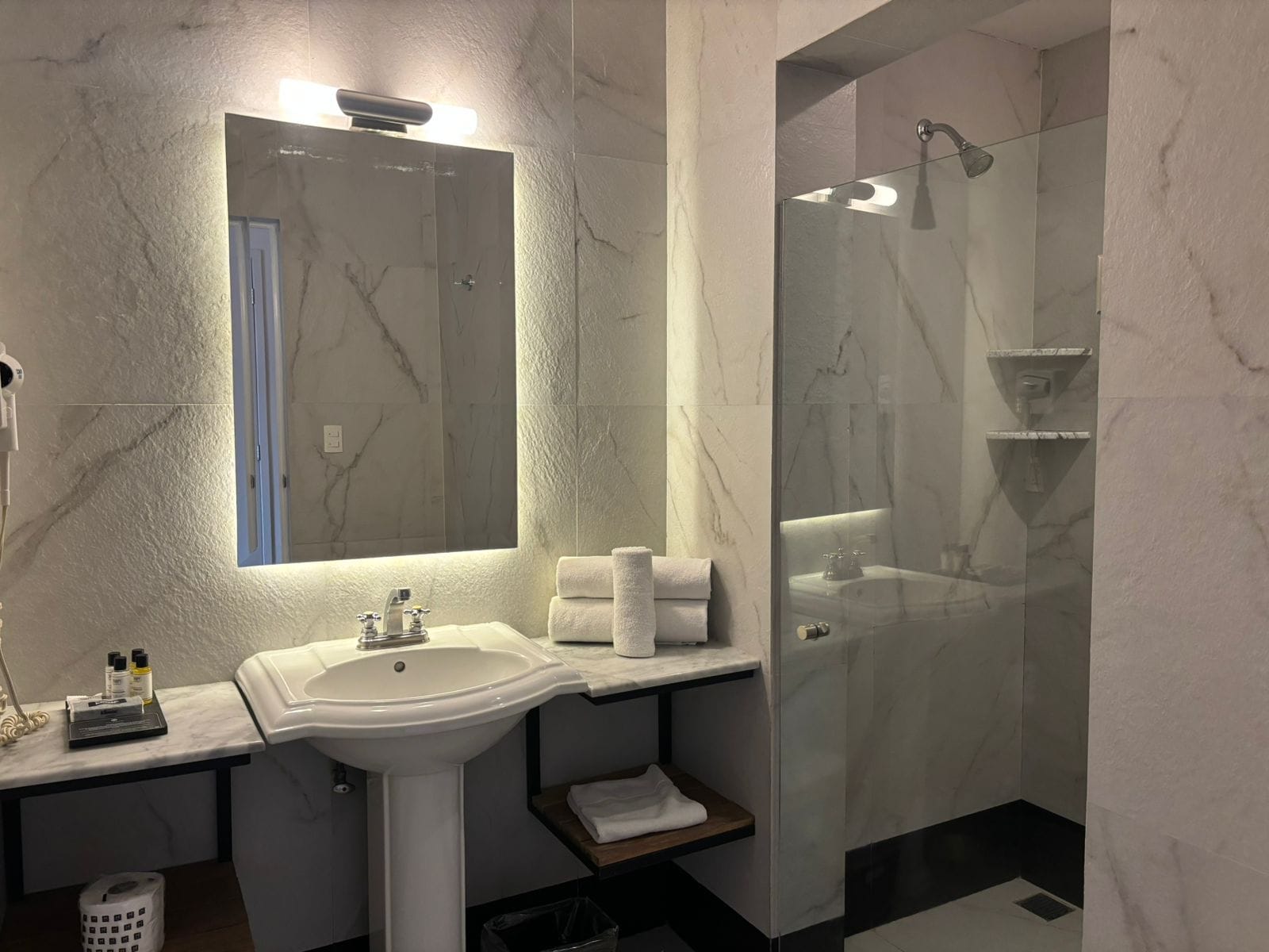 A modern bathroom with a marble sink, a glass-enclosed shower, and a large mirror.
