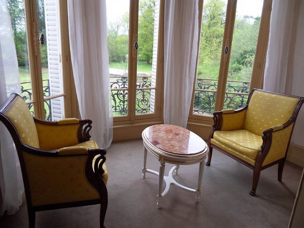 Een kamer met twee gele fauteuils, een tafel met een marmerblad en uitzicht op groen door grote ramen.