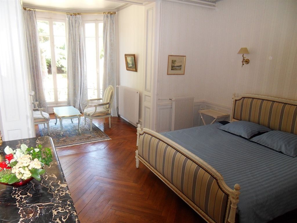 A bedroom with a bed, a table with flowers, a chair, a radiator, and a window with curtains.