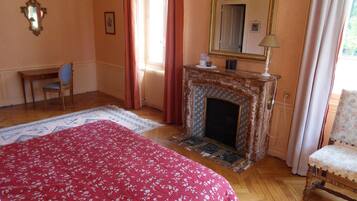 Un dormitorio con chimenea, una cama con colcha floral, una silla y un espejo en la pared.