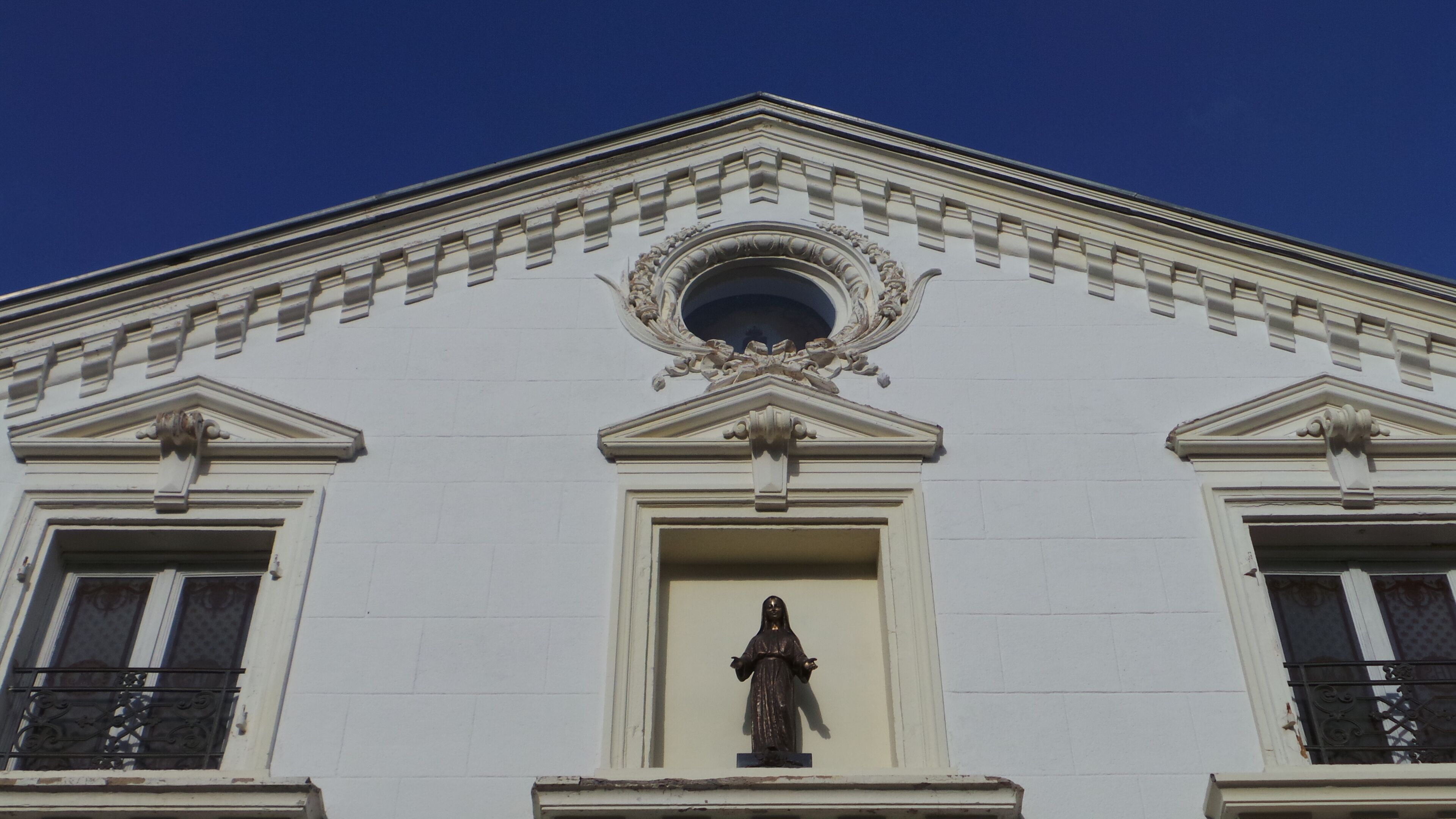 Un edificio de estilo arquitectónico clásico, con una estatua central, ventanas simétricas y molduras decorativas.