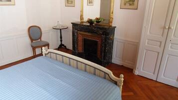 Un dormitorio con una cama, una silla, una mesita, una chimenea y una puerta.