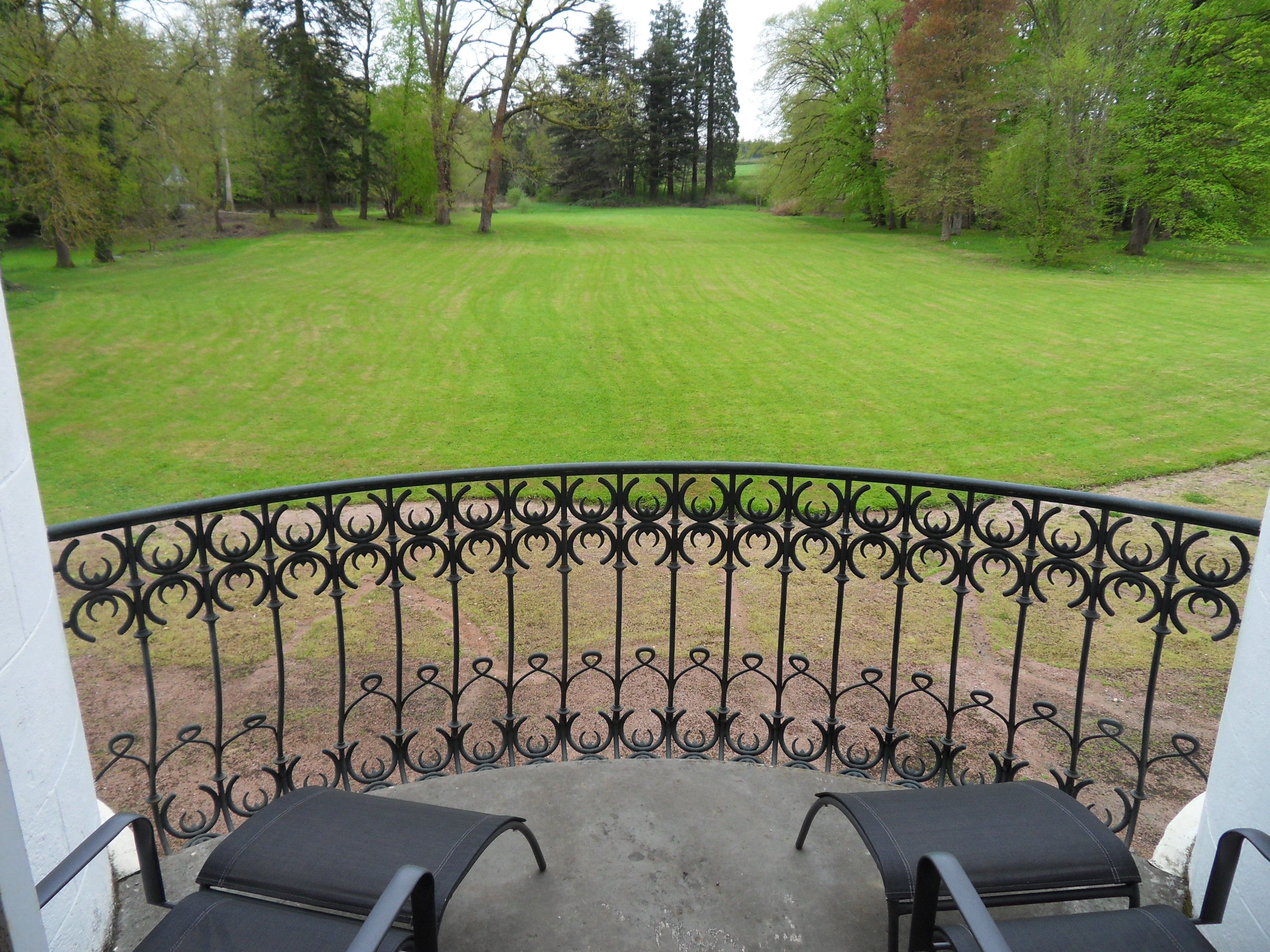 Un balcon doté d’une balustrade en fer forgé, donnant sur une pelouse bien entretenue et des arbres.