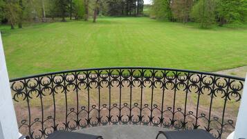 Un balcon doté d’une balustrade en fer forgé, donnant sur une pelouse bien entretenue et des arbres.
