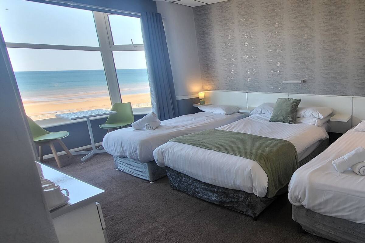 Een hotelkamer met twee bedden, een bureau en uitzicht op het strand.