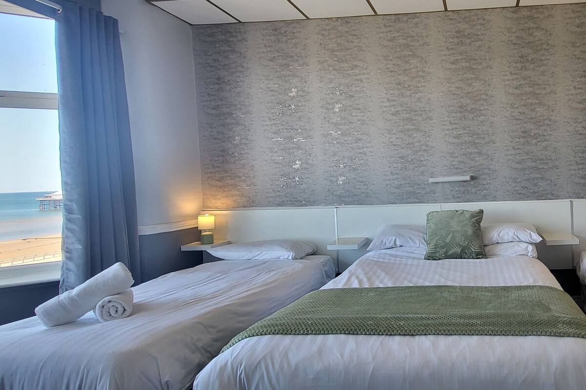 Een hotelkamer met twee bedden, uitzicht op het strand en een gestructureerde grijze muur.