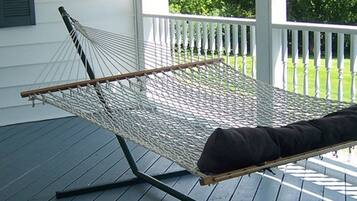 A hammock chair on a porch with a white railing and a grassy yard in the background.