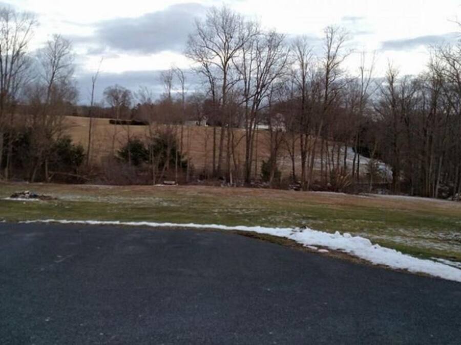 A parking lot with snow patches and leafless trees in the background.