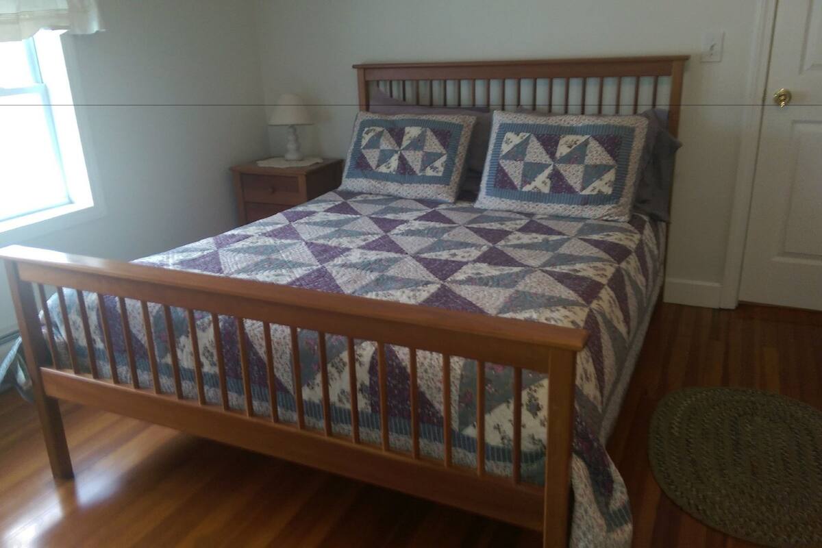 A bedroom with a wooden bed, a nightstand, a lamp, and a view of the outside.