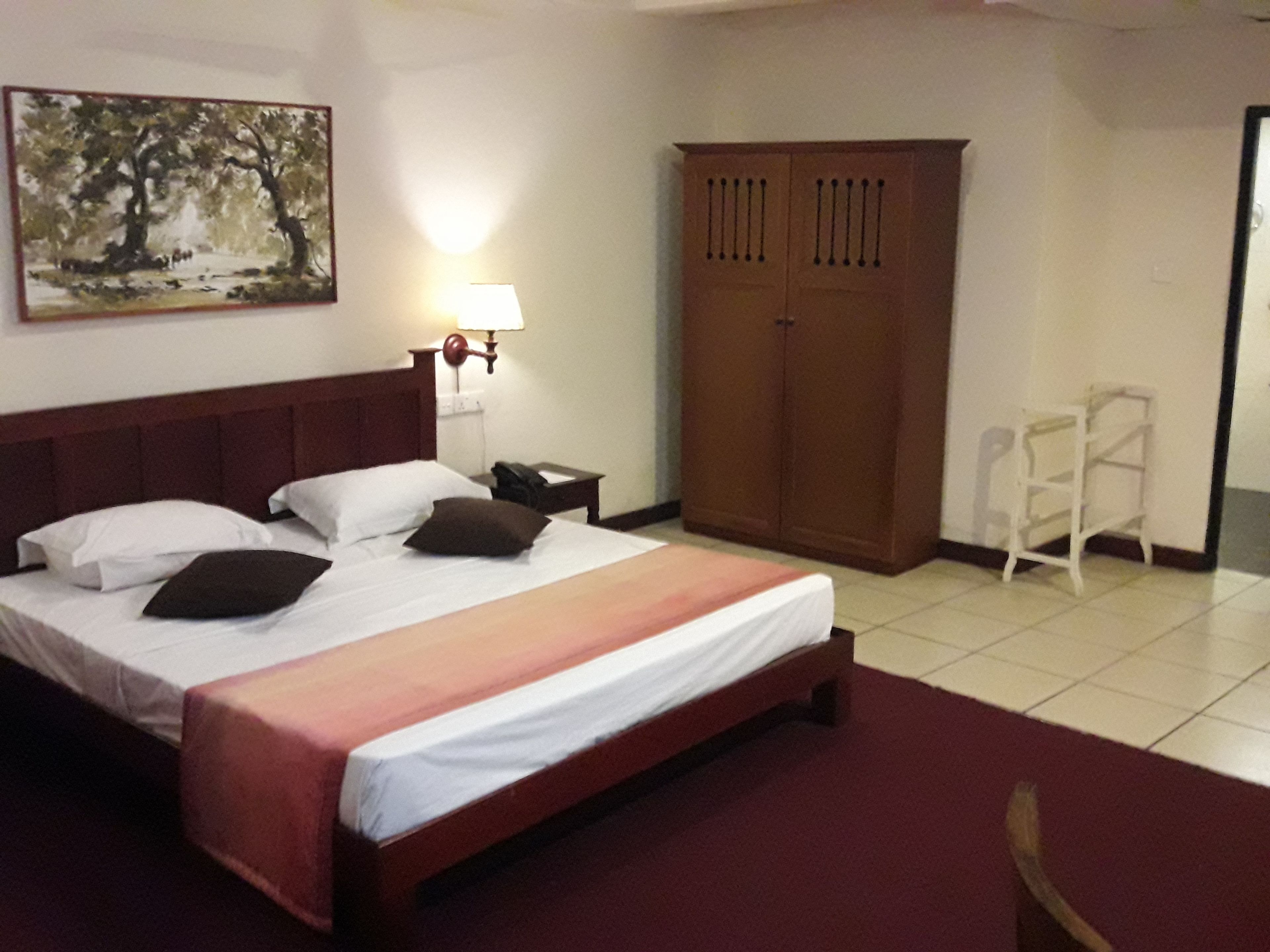 Quarto de hotel com cama, mesa de cabeceira, abajur, guarda-roupa e um quadro na parede.