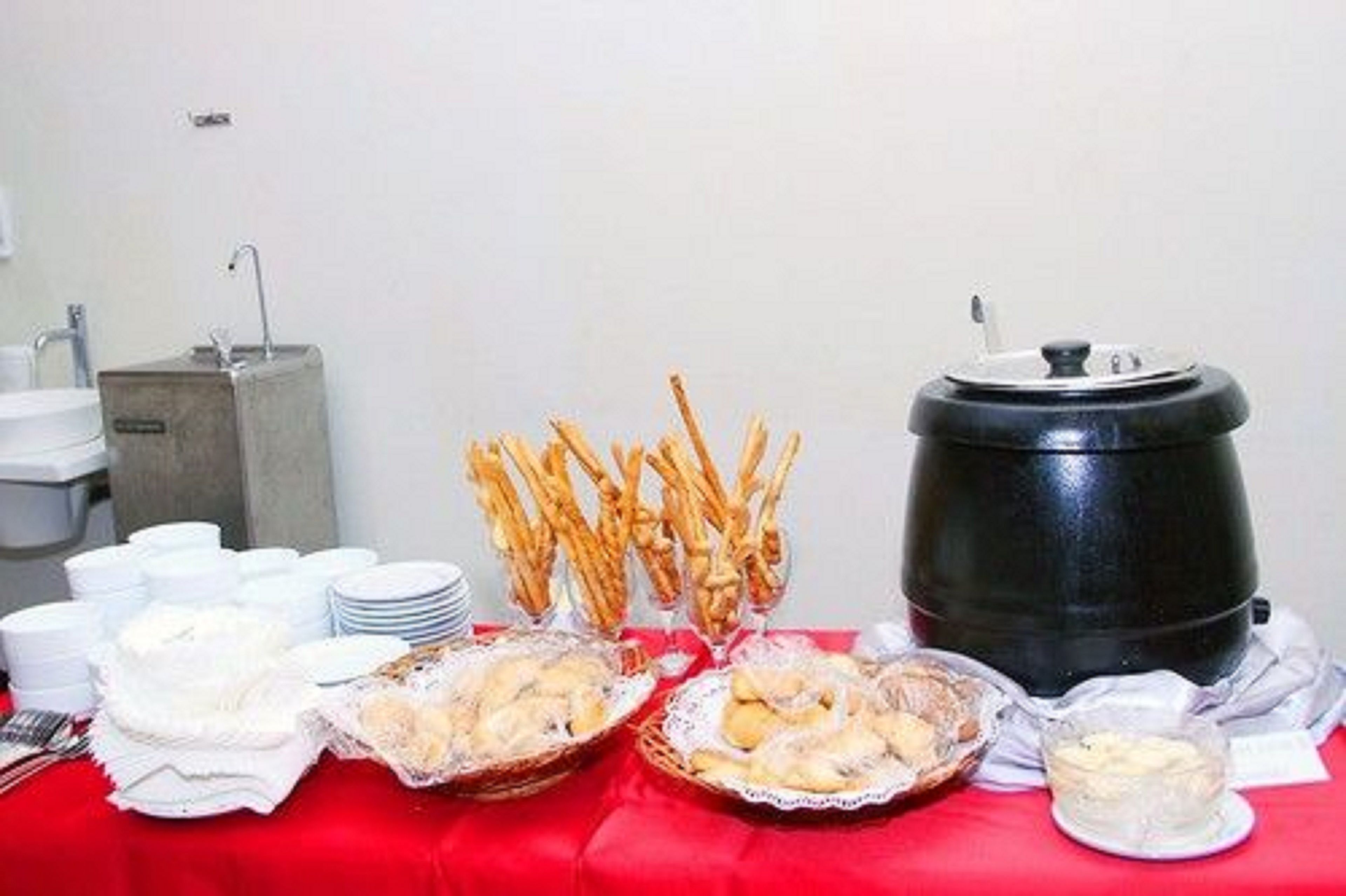 Een buffet met diverse gerechten, waaronder broodstengels, gebak en een drankdispenser.