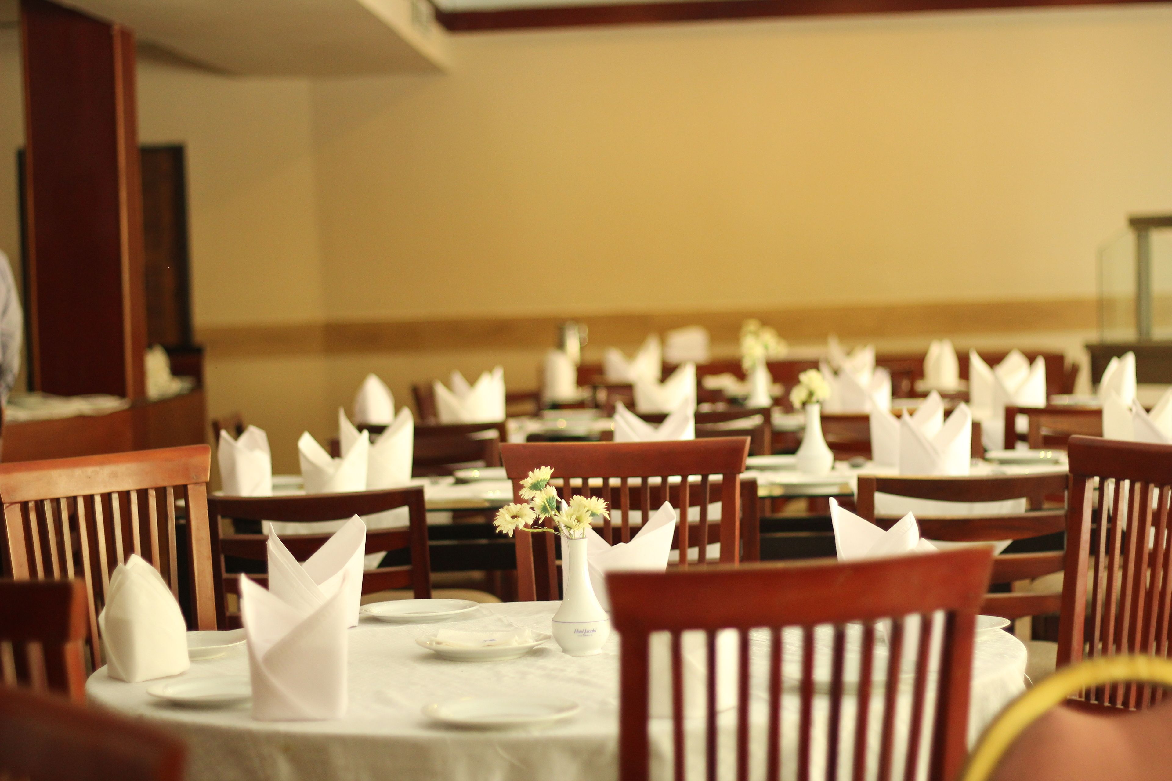 Un restaurant amb diverses taules preparades, totes amb mantells blancs, tovallons doblegats i un ram de flors.