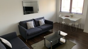 Un salon moderne avec un canapé gris, une table basse en verre et un coin repas avec des chaises blanches.