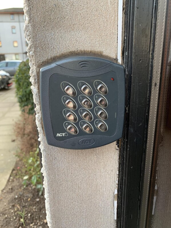 Cerradura electrónica en una pared color beige, con el marco de una puerta visible a la derecha.
