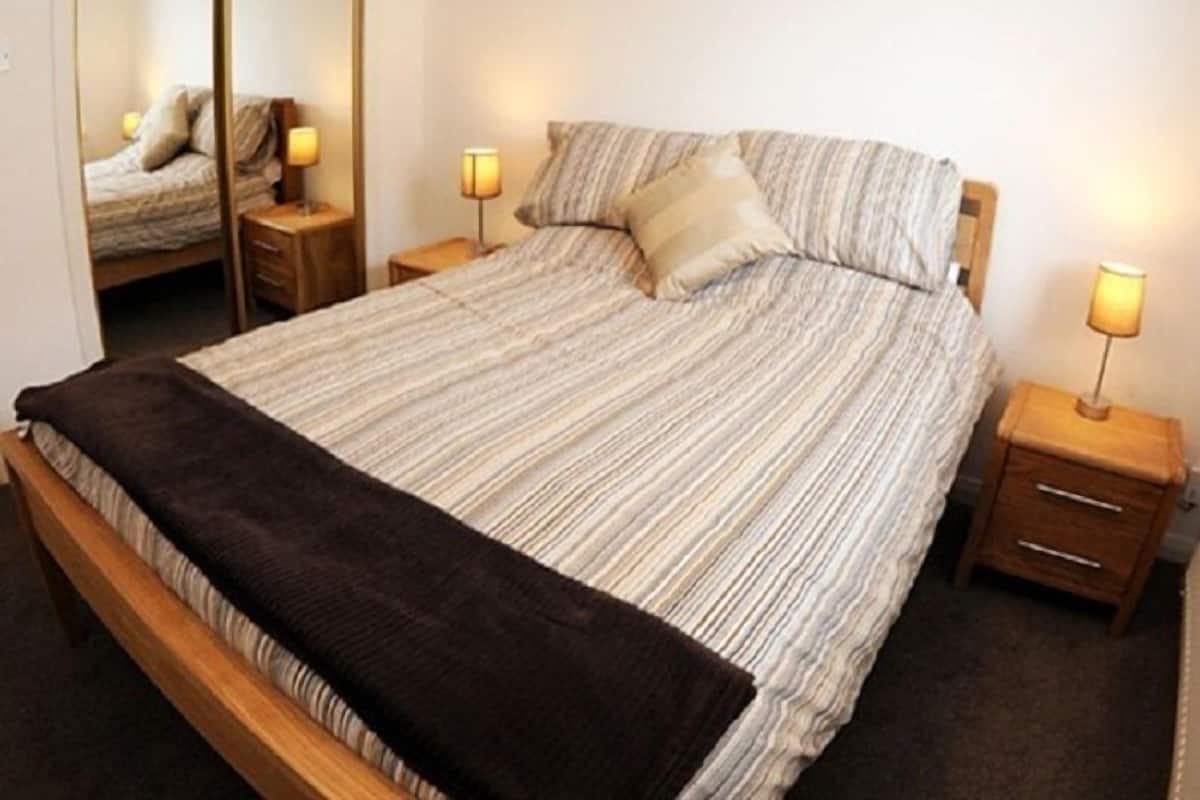A neatly made bed with a striped bedspread, two bedside tables with lamps, and a mirror on the wall.