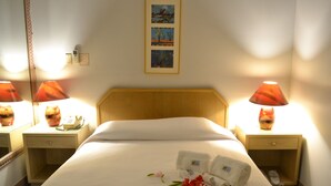 A hotel room with a neatly made bed, two bedside lamps, a nightstand with a phone, and a framed picture on the wall. - West Plaza Hotel Desekel (Koror)