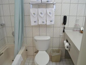 Ein Badezimmer mit Toilette, Dusche, Mülleimer, Handtuchhalter mit Handtüchern und Telefon an der Wand.
