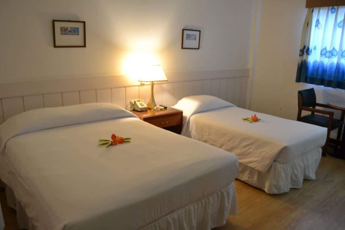 Ein Hotelzimmer mit zwei Betten, einem Nachttisch mit Lampe, einem Sessel und einem Schreibtisch.