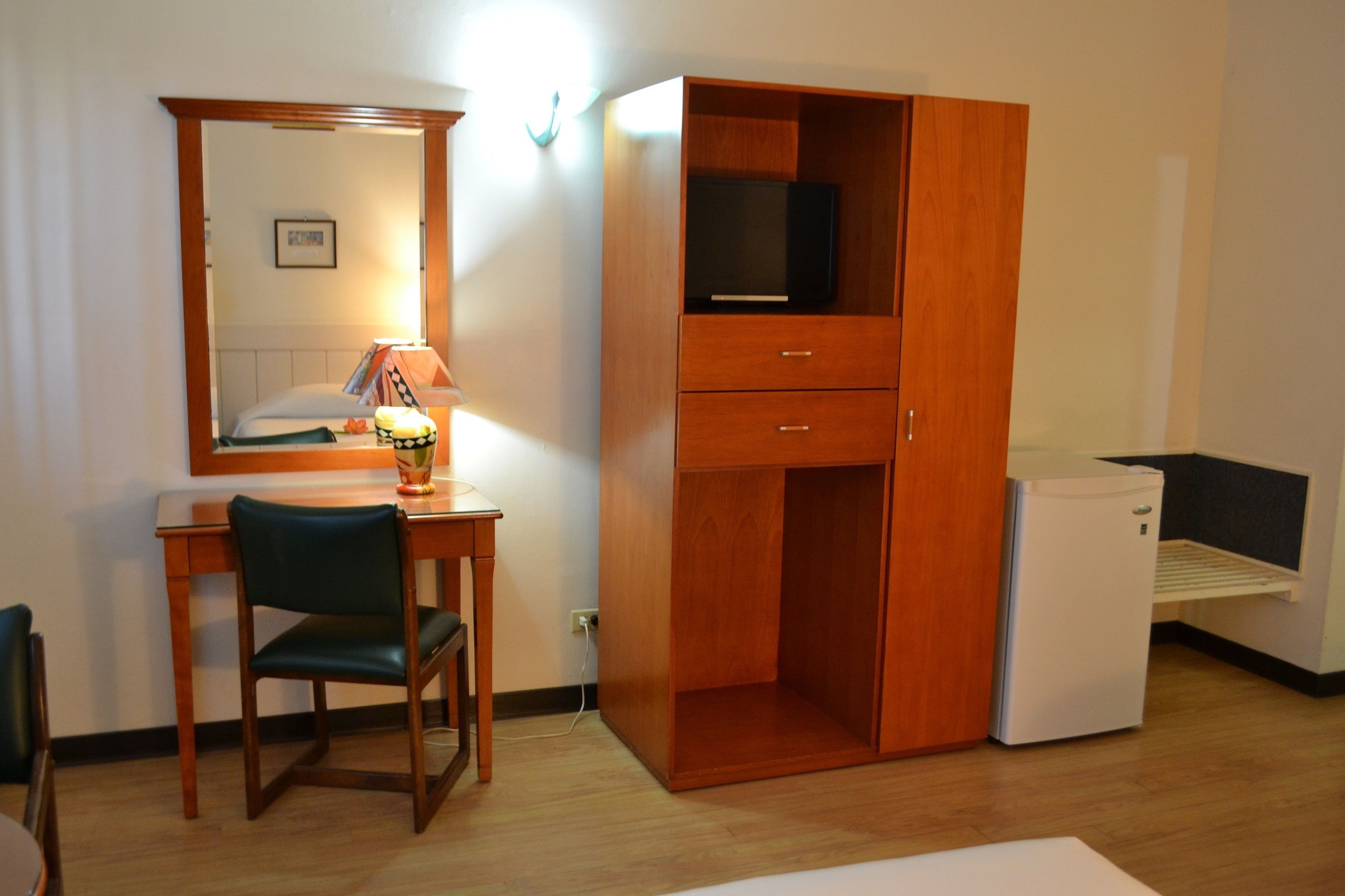 Habitación de hotel con escritorio de madera, una silla, armario, televisor y mini refrigerador.