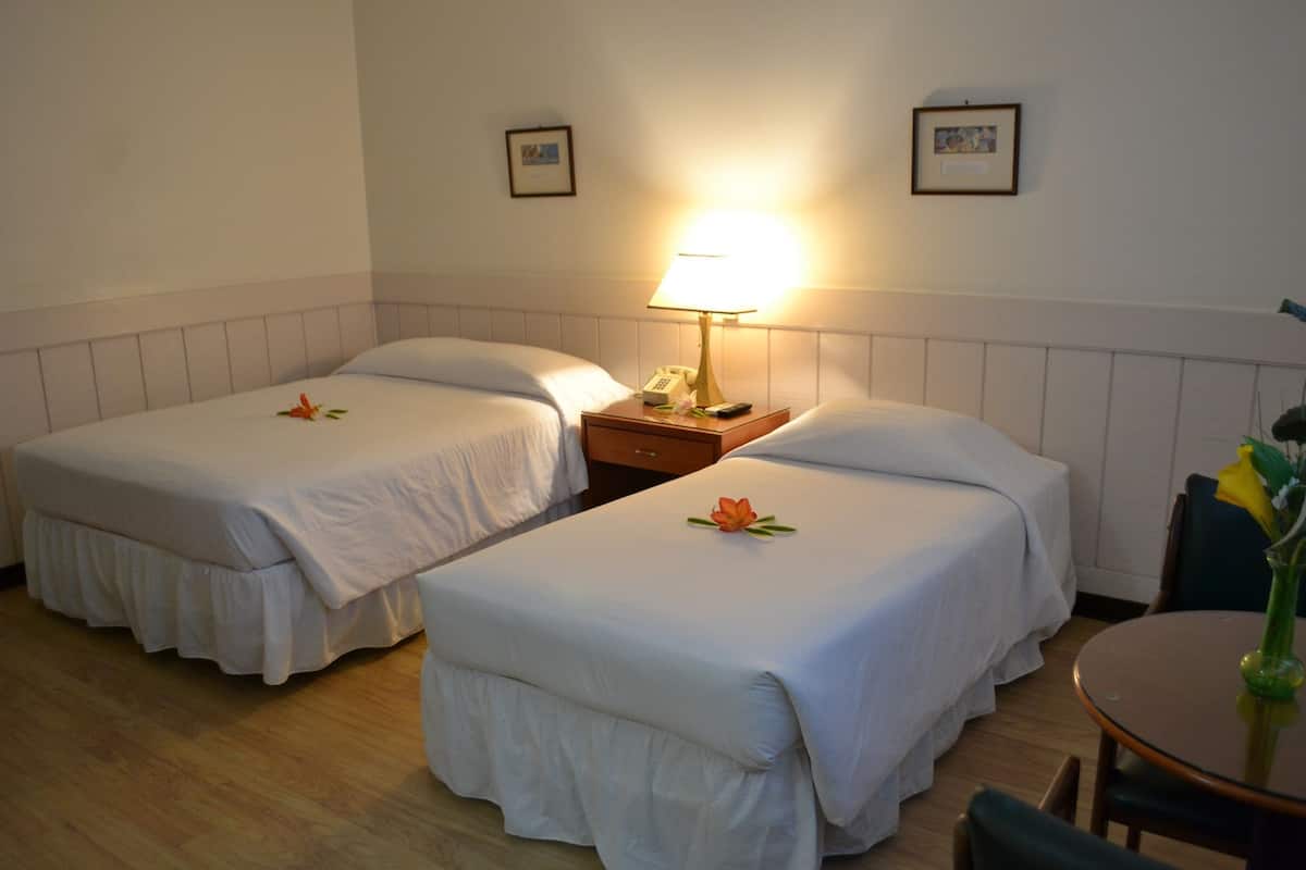 Ein Hotelzimmer mit zwei Einzelbetten, einem Nachttisch mit Lampe, einem kleinen Tisch mit Vase und einem Sessel.