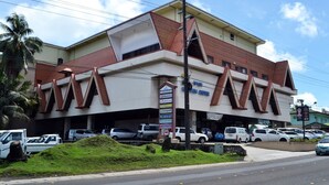Un immeuble à plusieurs étages doté d’un toit triangulaire au design original, d’une enseigne portant divers noms commerciaux et d’un parking où sont stationnées plusieurs voitures.