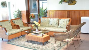Un salon avec des meubles en osier, une table basse en verre et un tapis à motifs.