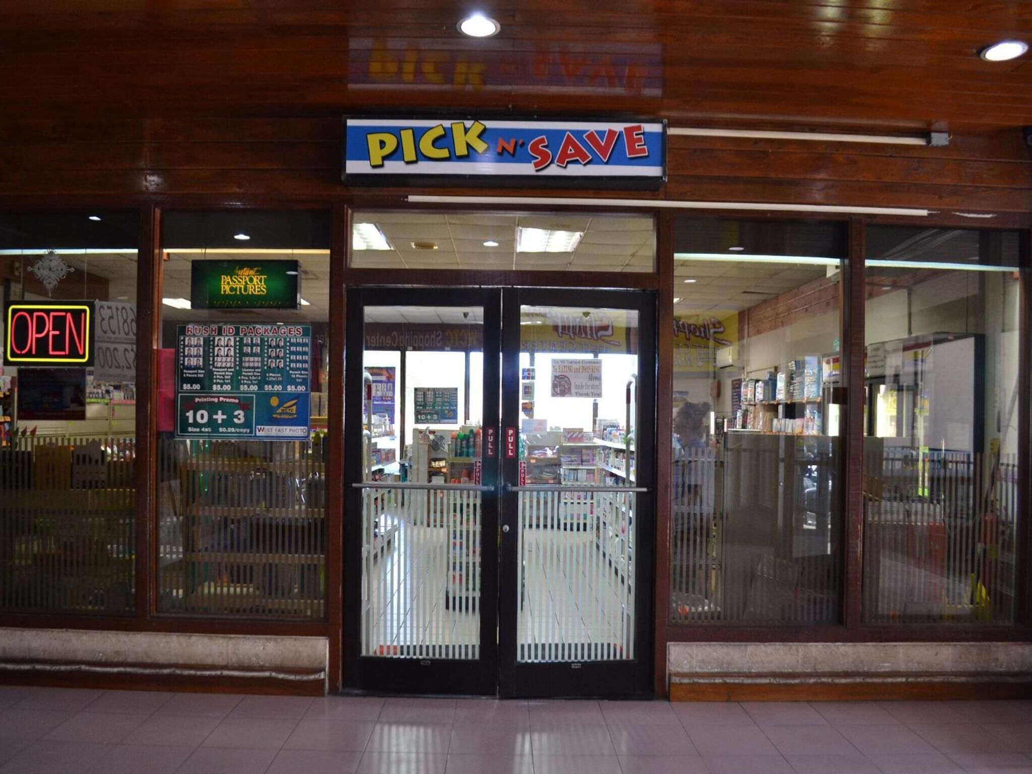 A storefront with a 'PICK N SAVE' sign, a 'Passport Pictures' sign, and a 'RUSH ID PACKAGES' sign.