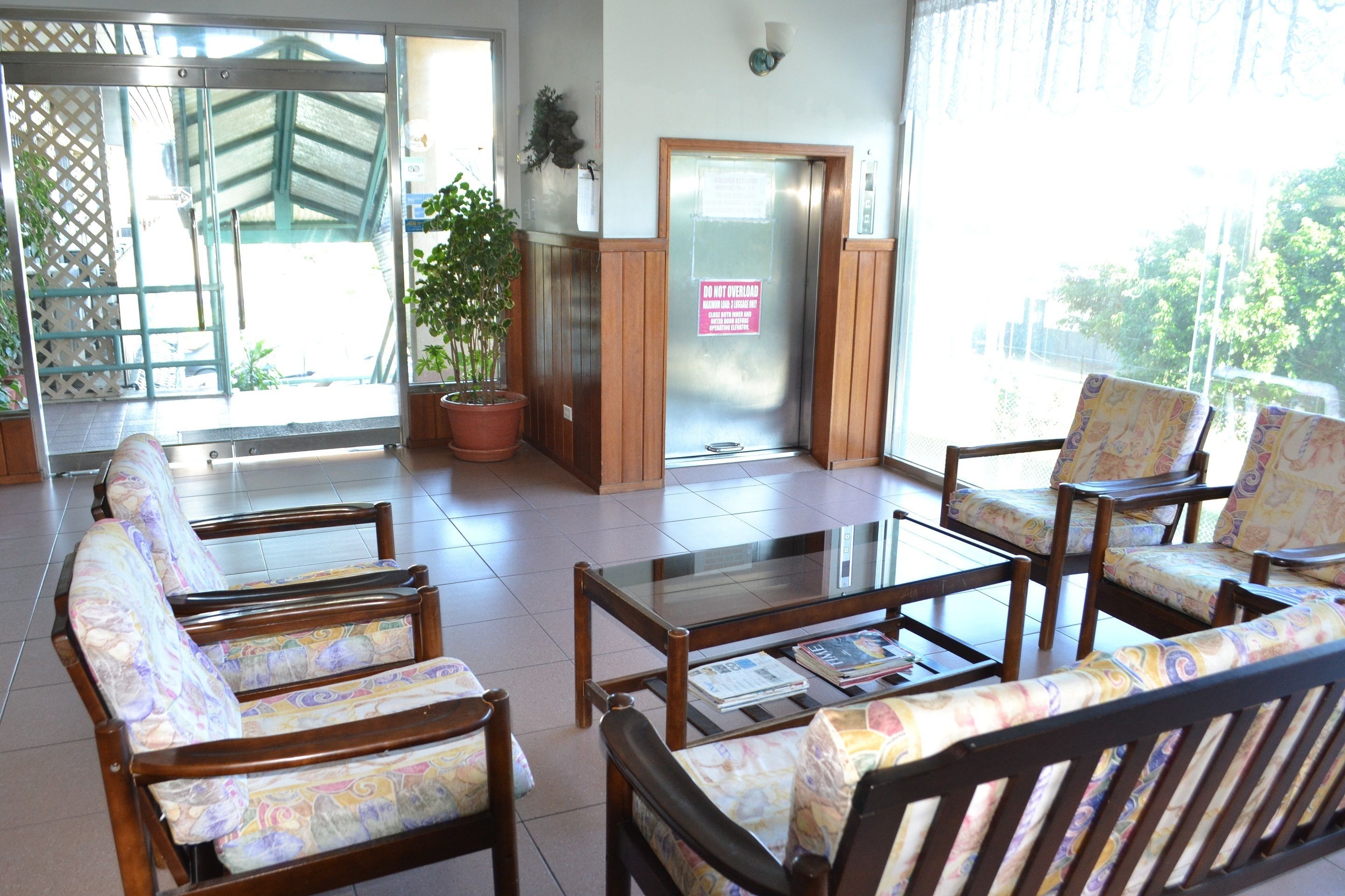 Un área de recepción con sillas de madera, una mesa con cubierta de vidrio y una planta en maceta.