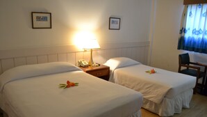Une chambre d’hôtel avec deux lits simples, une table de chevet avec une lampe, une chaise et un bureau.