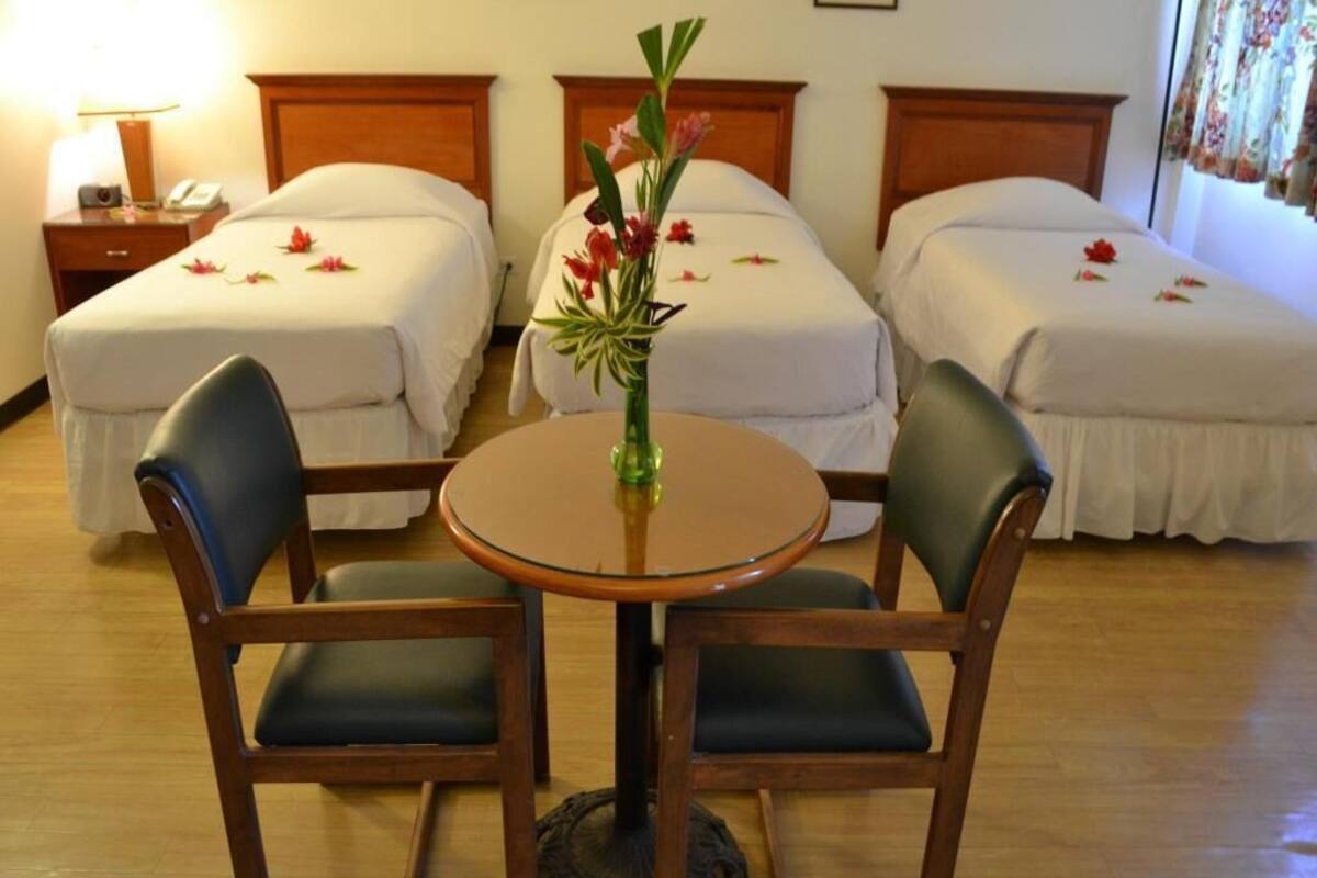 A hotel room with two beds, a round table with chairs, and a vase with flowers.