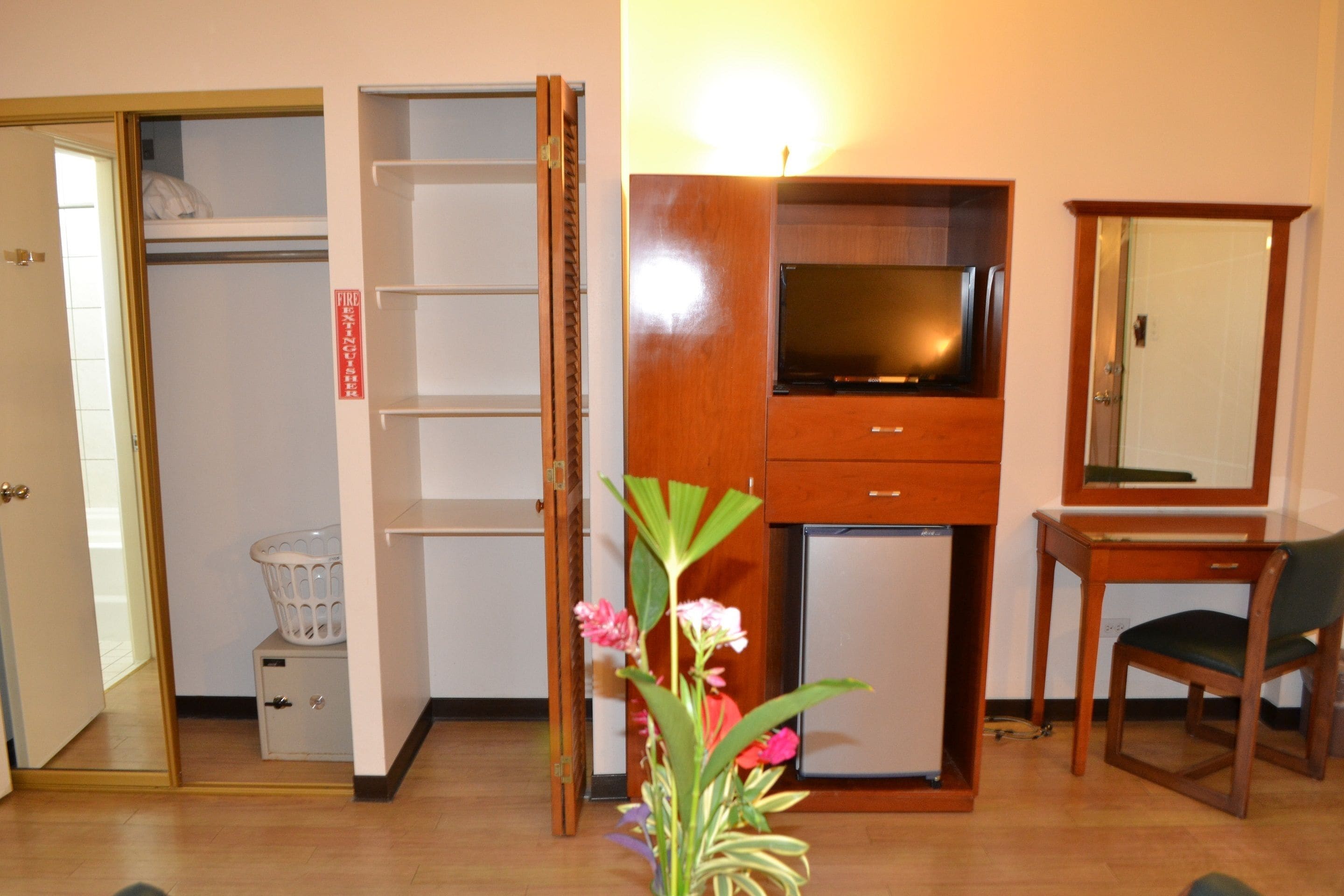 A room with a wooden cabinet, a television, a desk with a chair, and a mirror.