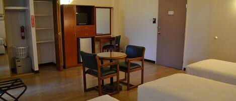 A hotel room with two beds, a desk with a chair, a television, and a wardrobe.