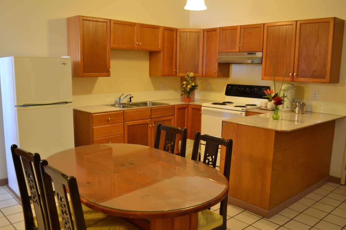 A kitchen with wooden cabinets, a refrigerator, a stove, a sink, and a dining table with chairs.