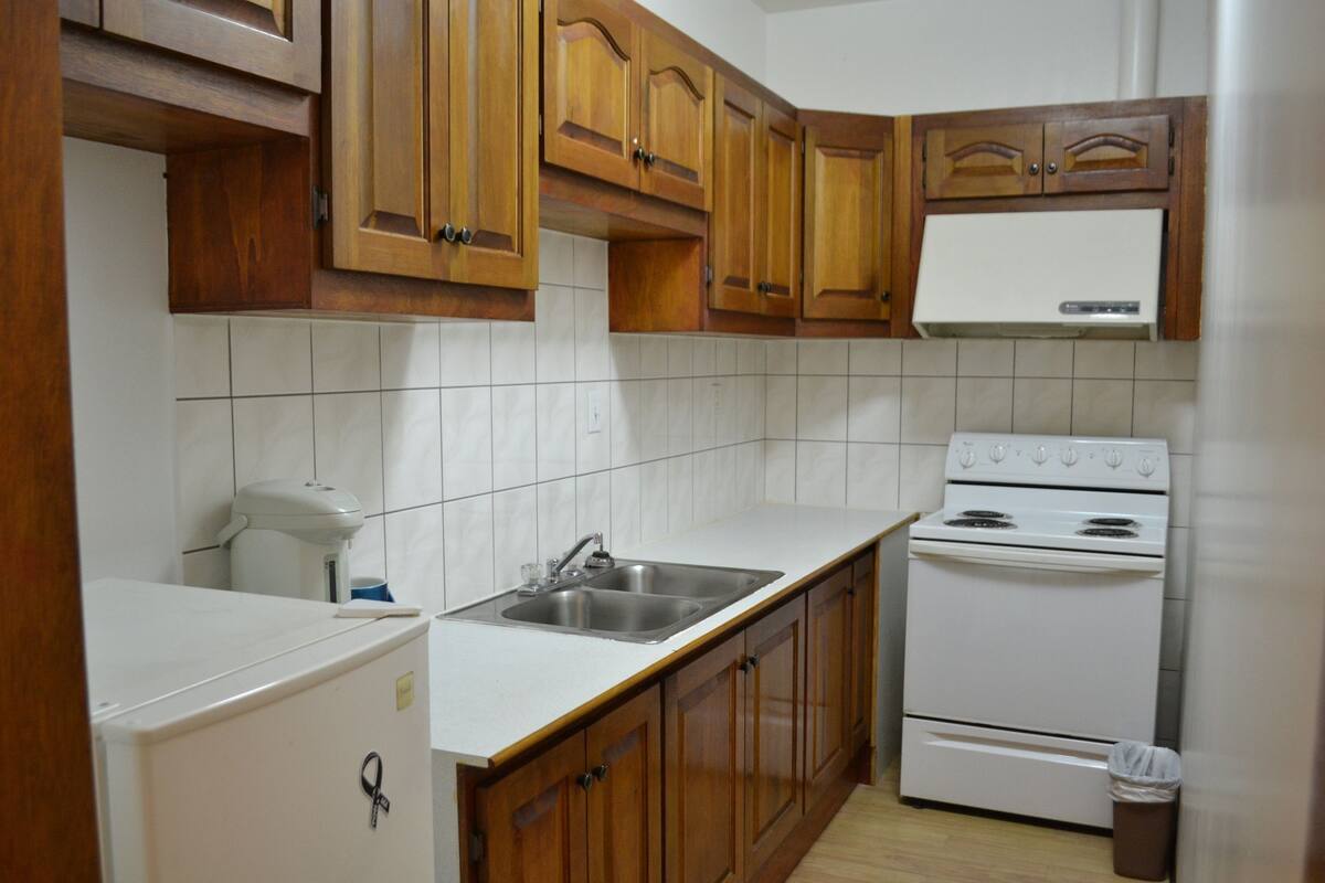A compact kitchen with wooden cabinets, a white countertop, a sink, and a white stove.