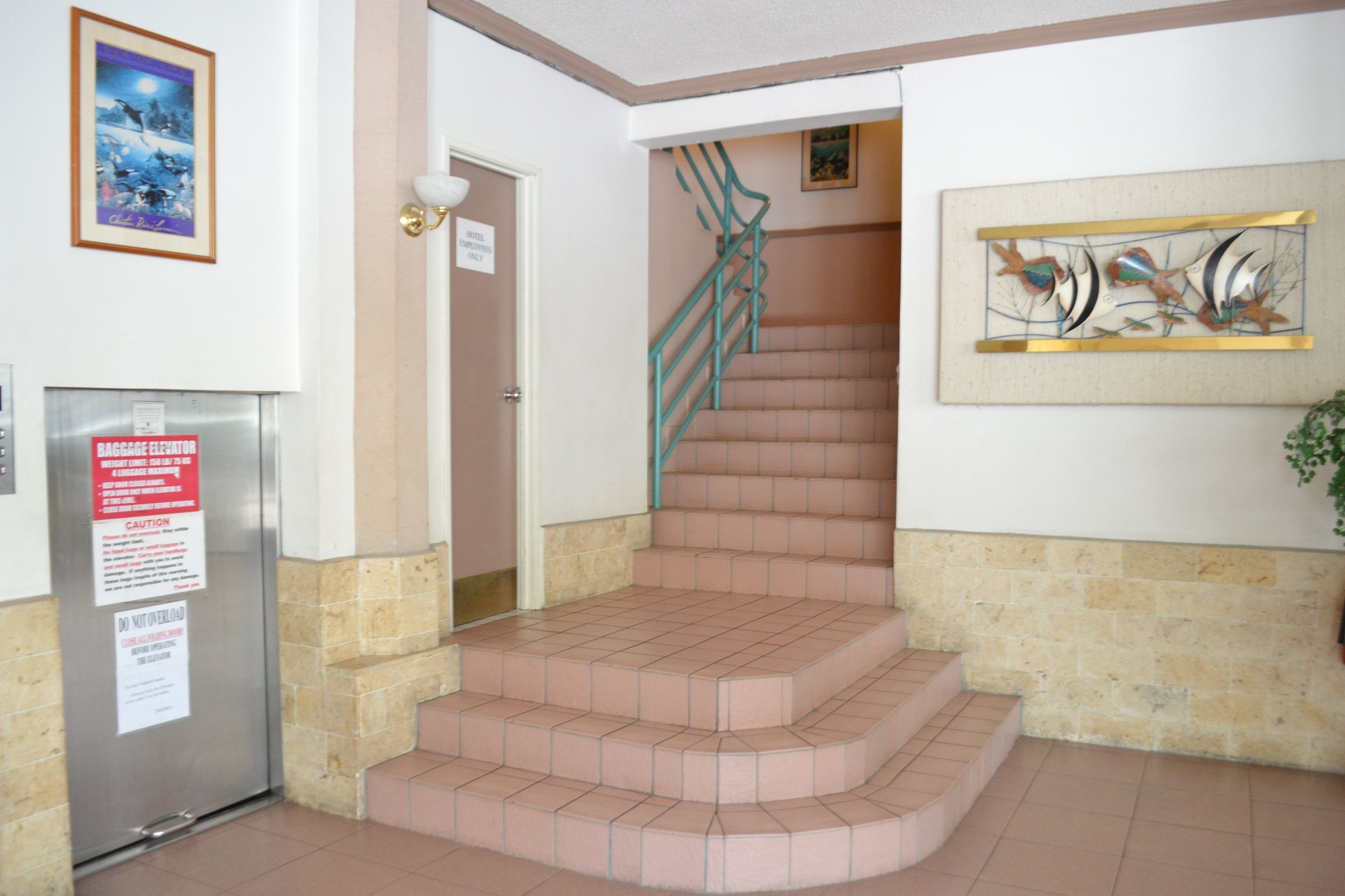 A hotel lobby with a staircase, a refrigerator, and a wall-mounted artwork.