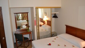 Hotellihuone, jossa on sänky, työpöytä tuolilla, peili, yöpöytä ja lamppu.