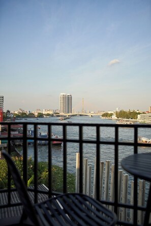 A view from a balcony overlooking a river with boats, a bridge, and buildings in the distance. - Baan Wanglang Riverside (Bangkok)
