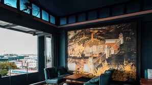 Een modern interieur met een groot muurschildering van een traditioneel gebouw, zitplaatsen en uitzicht over de stad.