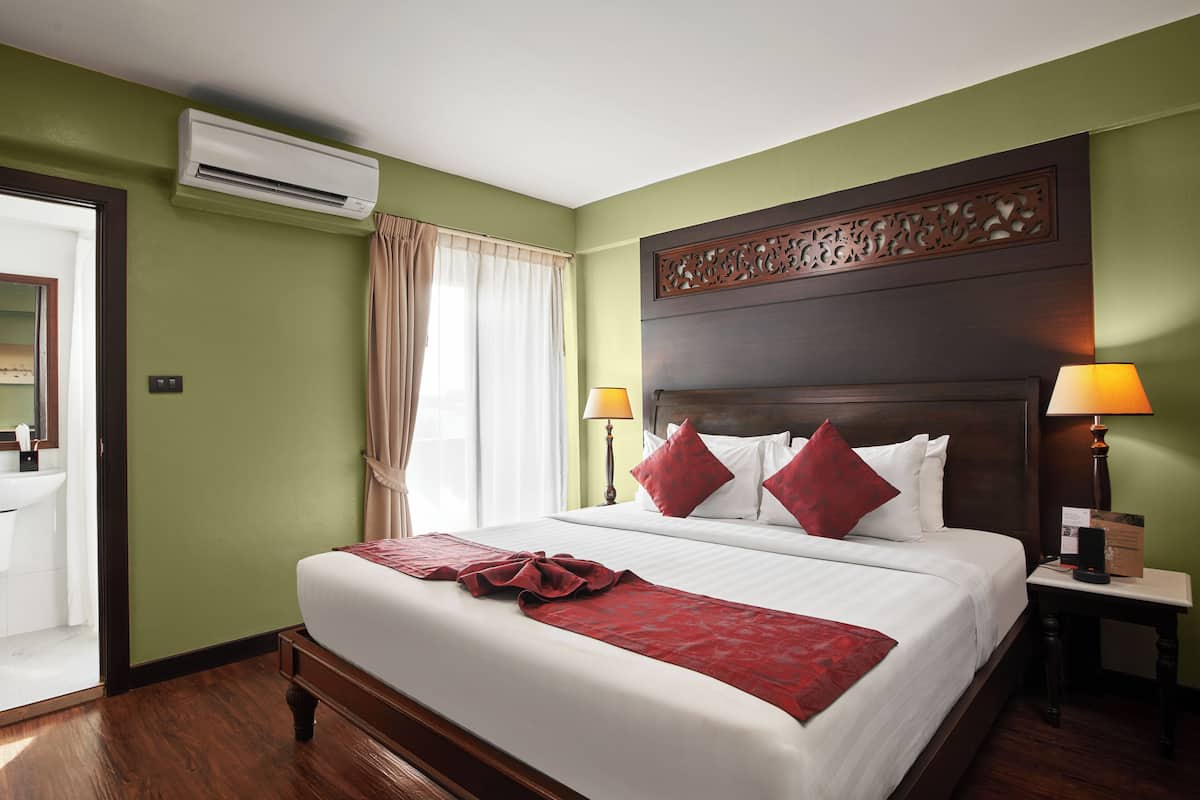 Quarto de hotel com uma cama grande, duas luminárias de cabeceira, um painel de cabeceira de madeira e um aparelho de ar condicionado.