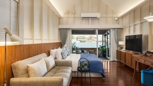 Een moderne hotelkamer met een bank, een klein tafeltje met een plant, een televisie en een balkon met uitzicht op het water.