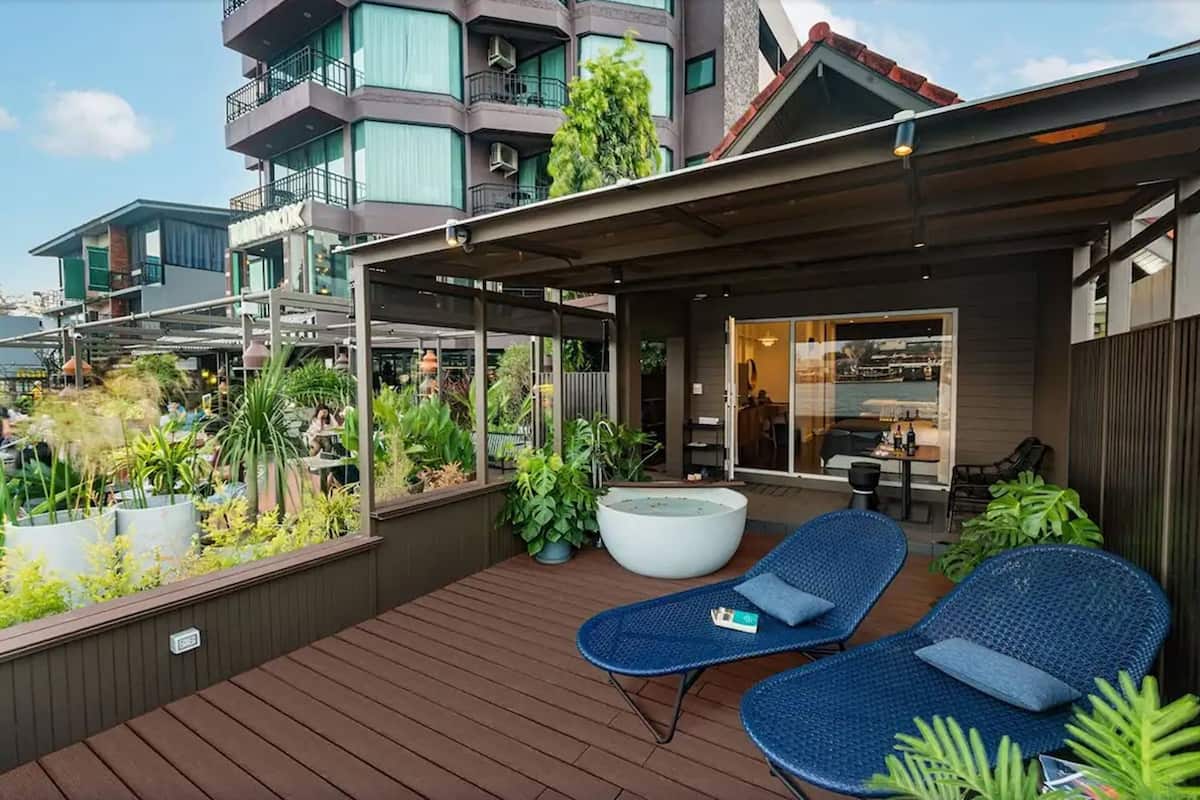 Terraço no telhado com duas cadeiras de descanso azuis, um vaso grande e uma área de refeições com mesas e cadeiras.