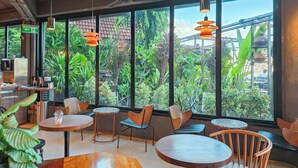 Een modern café met grote ramen, houten tafels en oranje hanglampen.