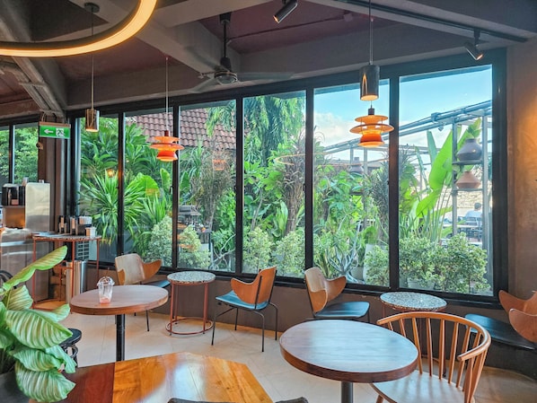 A modern cafe with large windows, wooden tables, and orange pendant lights. - Baan Wanglang Riverside (Bangkok)