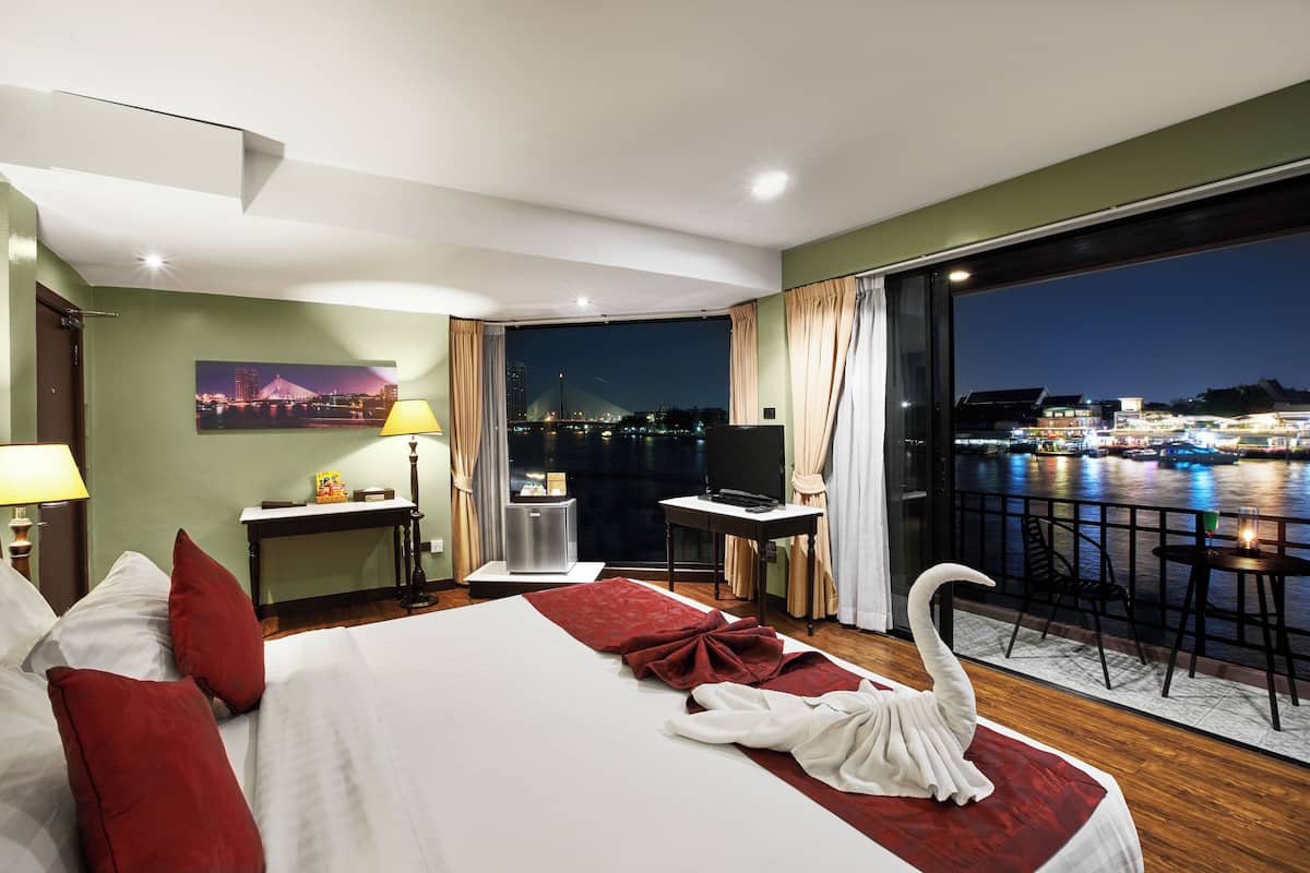 Quarto de hotel com uma cama grande, uma escrivaninha, uma cadeira, uma televisão e vista para a cidade à noite.