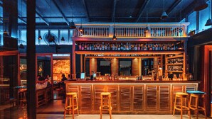 Een bar met houten krukken, een toonbank met flessen en een balkon.