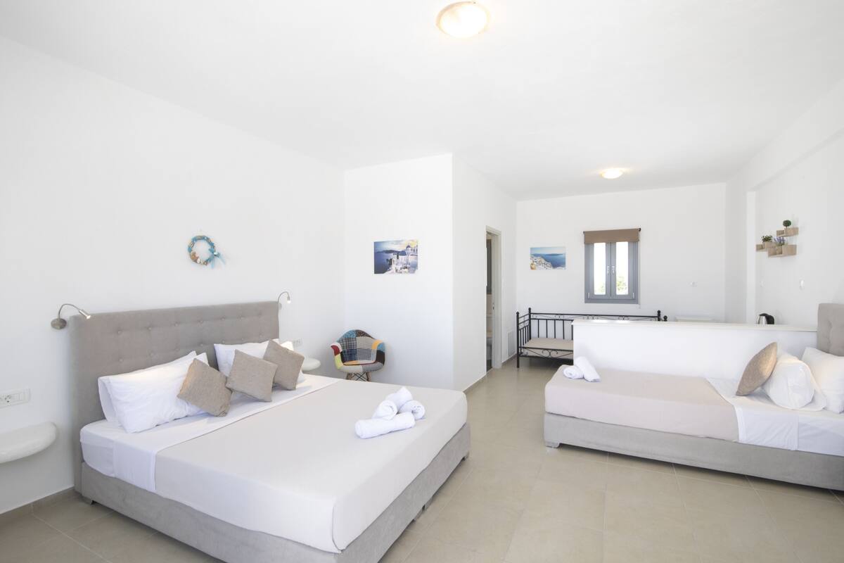 A hotel room with two beds, a small seating area, and a view of the sea.