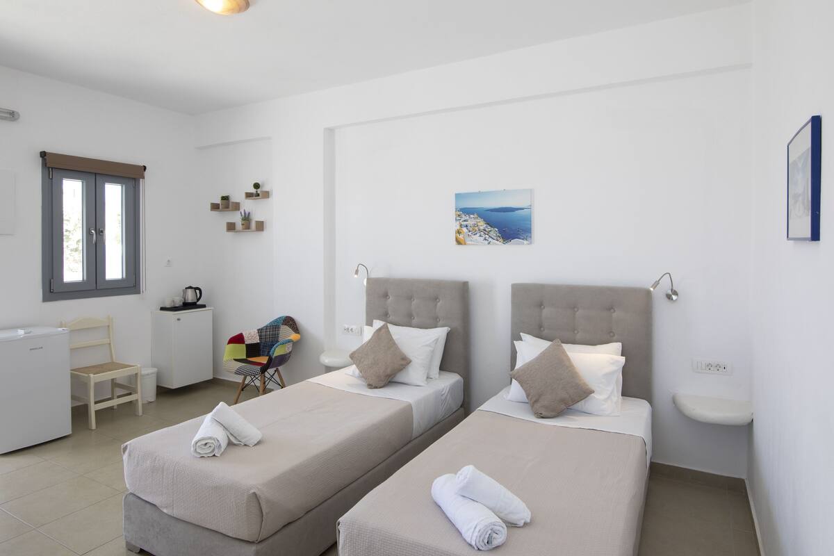 A clean, modern room with two beds, a desk, and a small kitchenette.