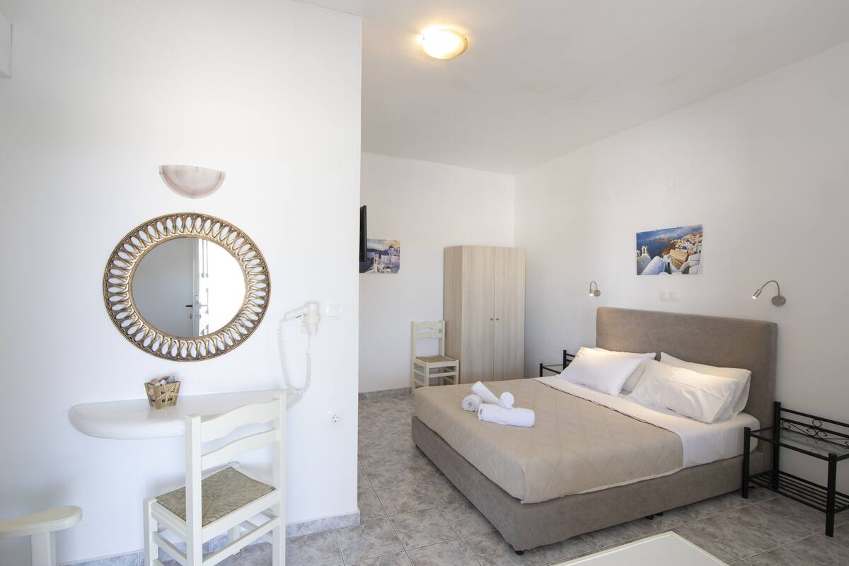 A bedroom with a bed, a bedside table, a chair, a mirror, and a wall-mounted light fixture.
