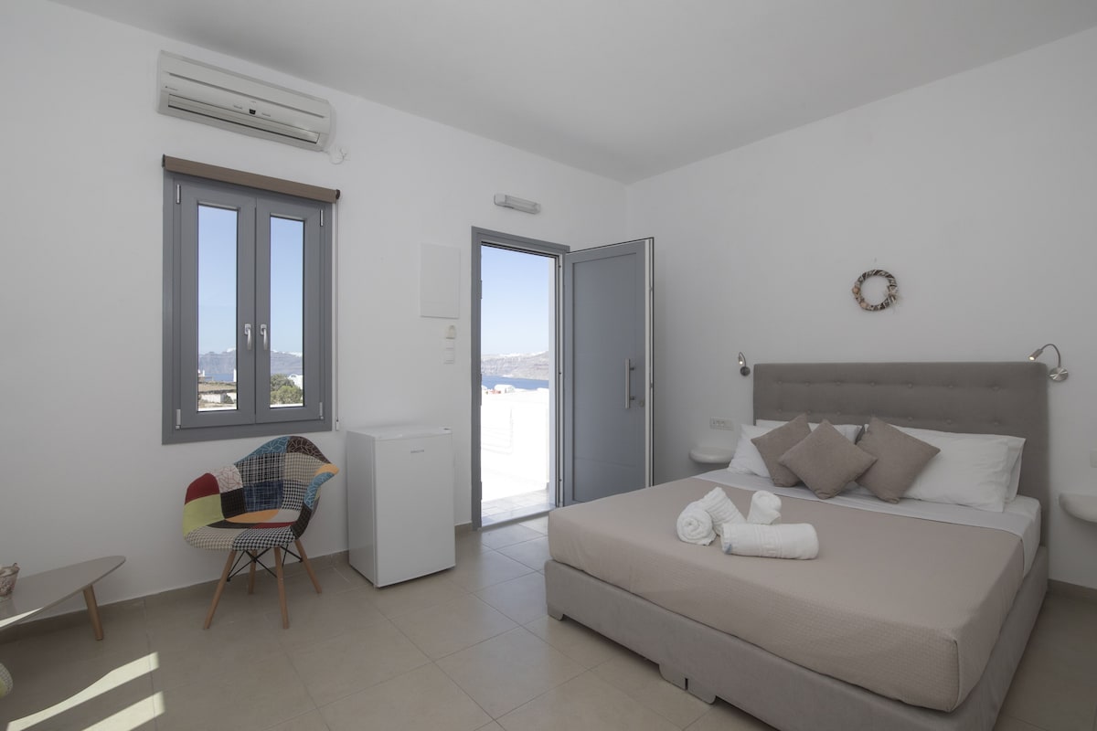 A bedroom with a bed, a chair, a window, and a view of the sea.