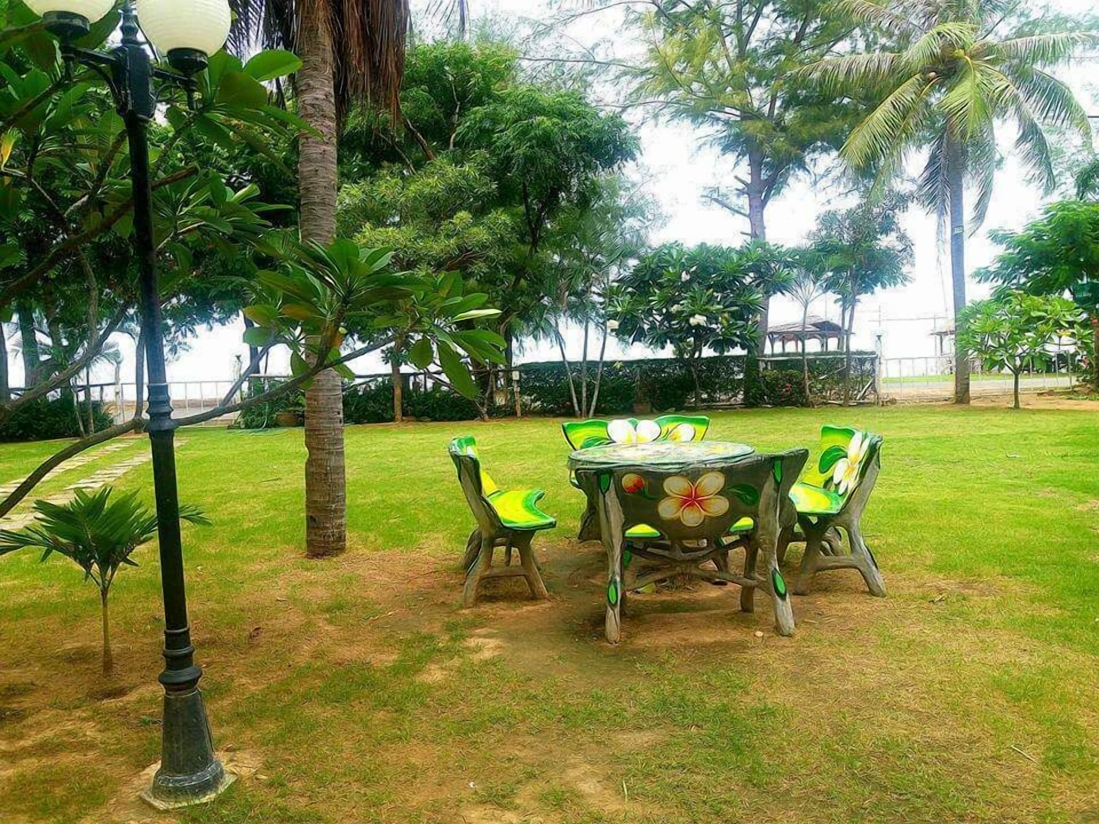 Un espace de restauration en plein air, avec une table et des chaises, entouré d’une végétation luxuriante et de palmiers.
